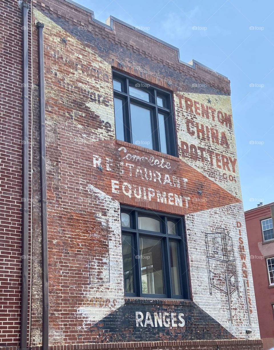 A side of an old building made of brick with faded paint and advertisements on it