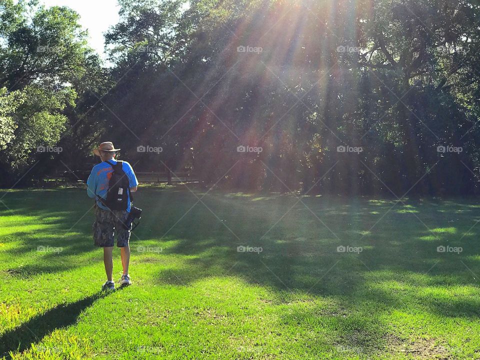 Man hiking through the woods in a rainbow of sunlight.