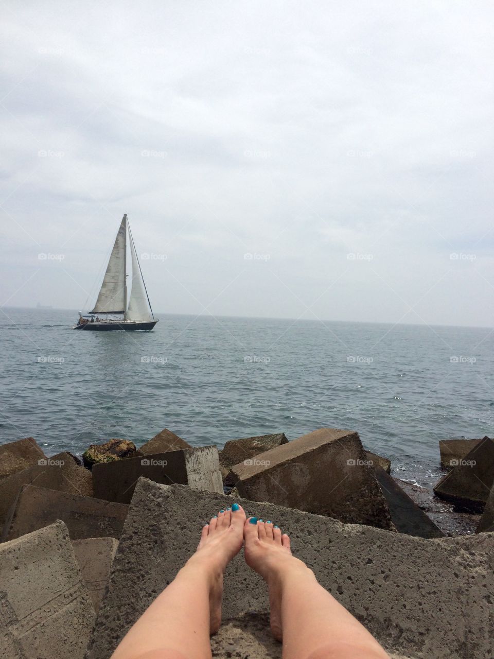 Sailboat on a cloudy day. Watching my the sailboats pass by on the rocks of the port in Alicante, Spain
