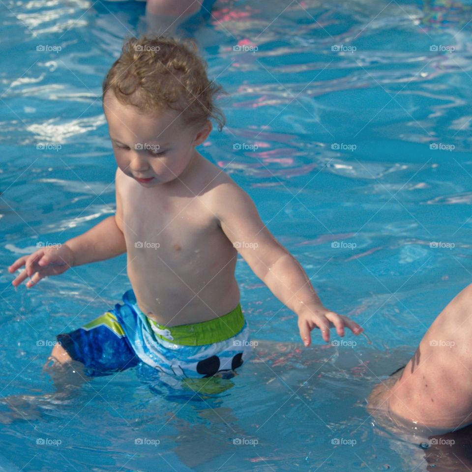 A toddler boy at the outdoor swimming pool for his first round of swimming lessons on a sunny summer evening. 