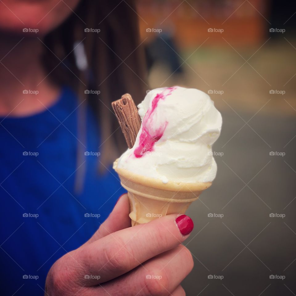 Woman with red nail varnish holding an ice cream cone. 