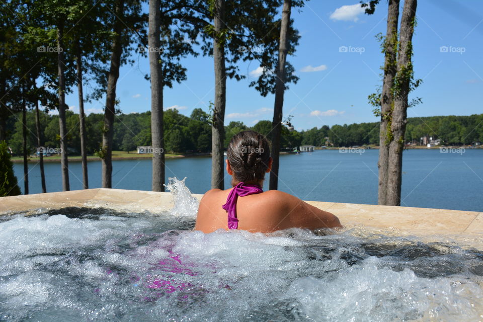 Female in hot tub with water jets on overlooking a lake