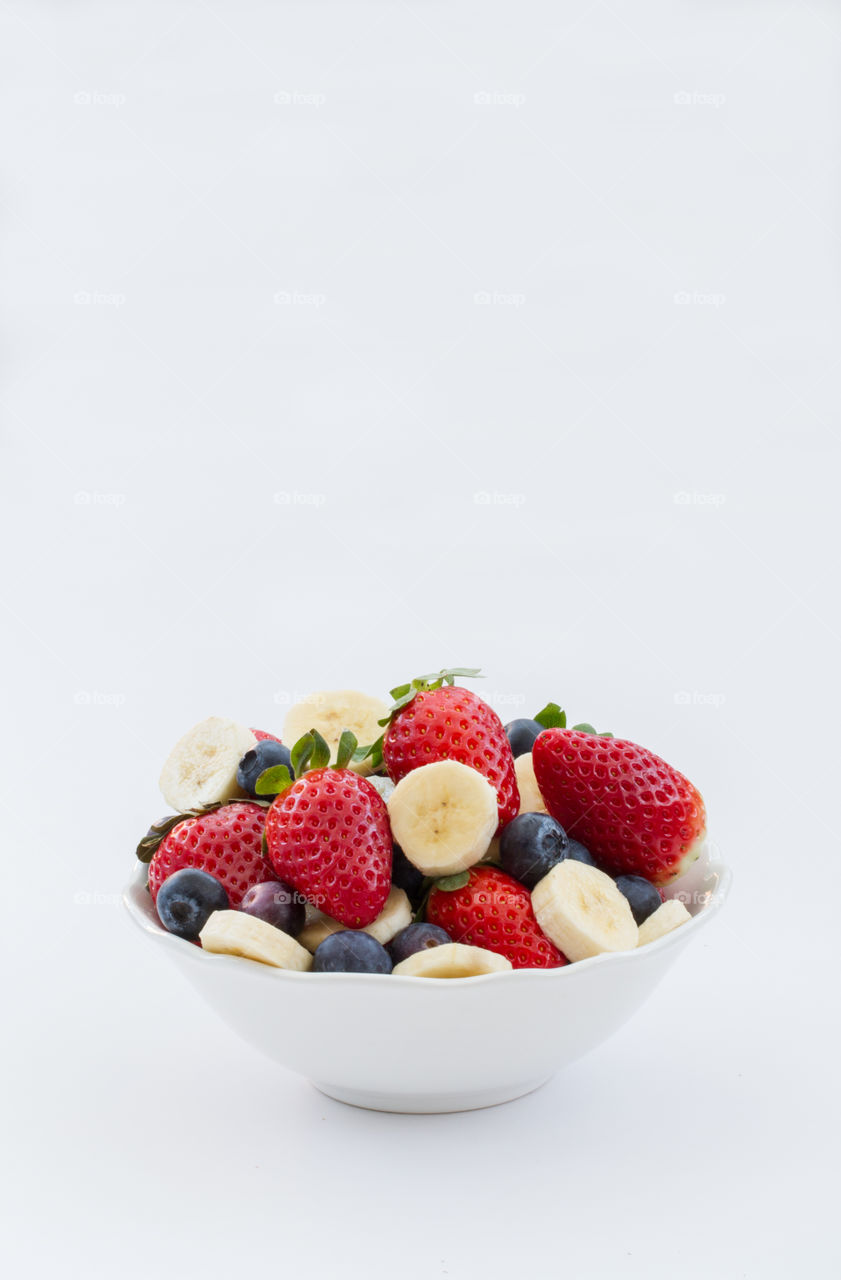 A bowl full of fresh fruit including strawberries, blueberries and bananas on an isolated white background. Delicious smoothie ingredients.