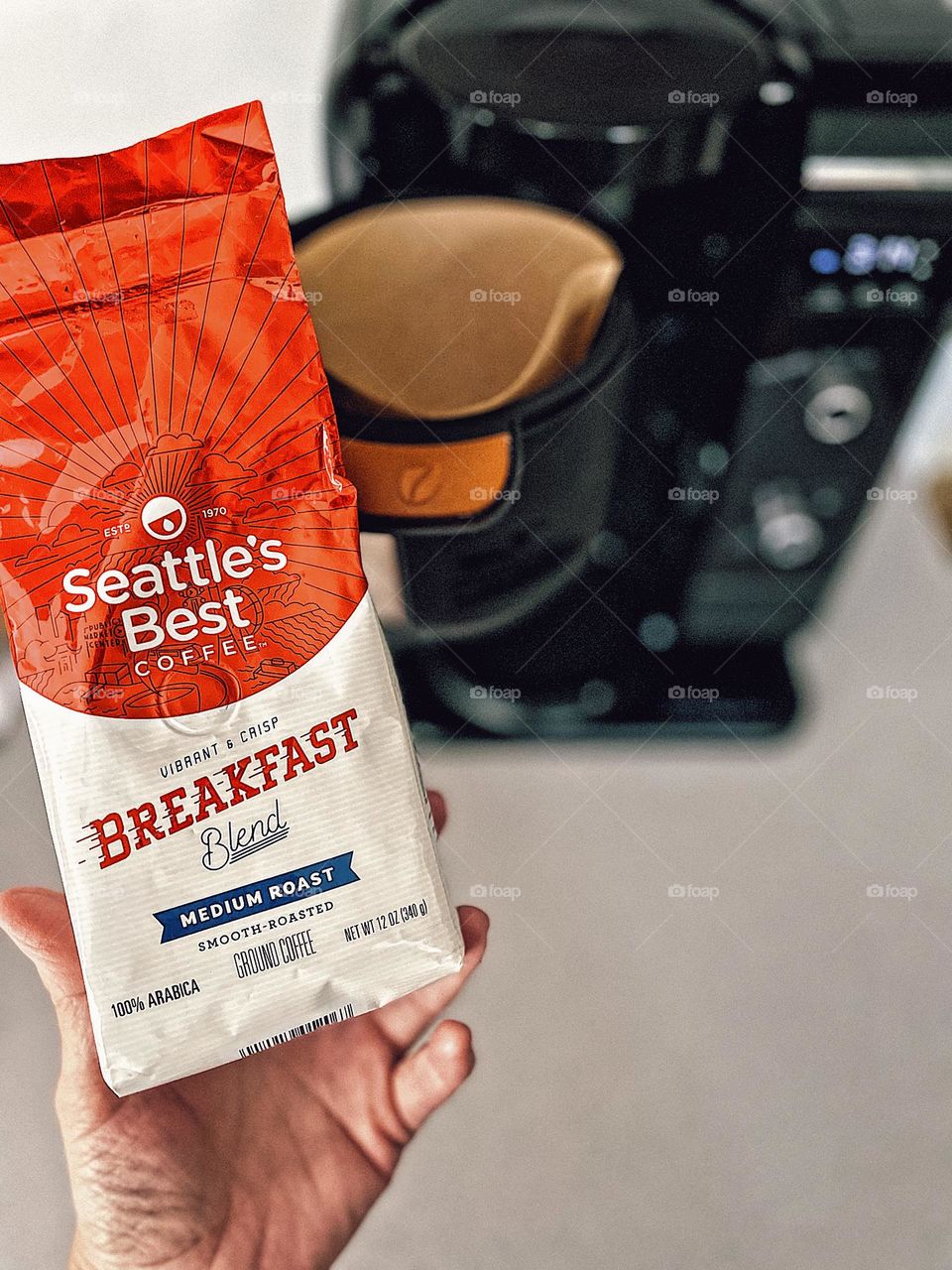 Making coffee in the morning, Seattles Best coffee Advertisement, caffeine in the morning, breakfast blend ground coffee, woman’s hand holding bag of Seattle’s Best ground coffee