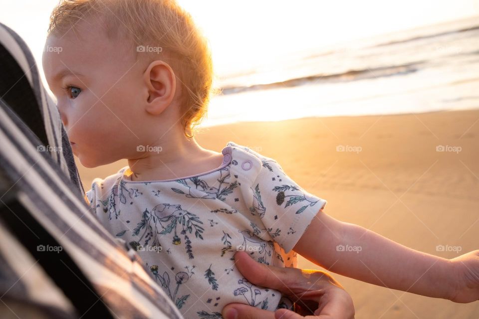 Close up of mother holding baby with sunrise beach on the background