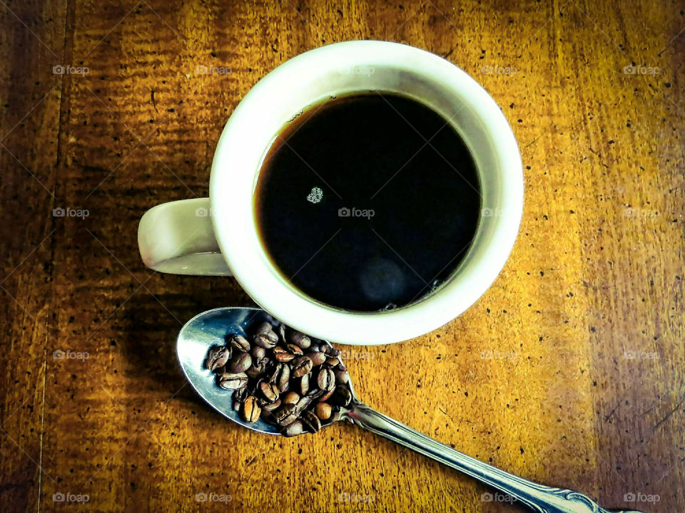 Fresh Cup Of Coffee And Spoonful Of Beans On Wood Table