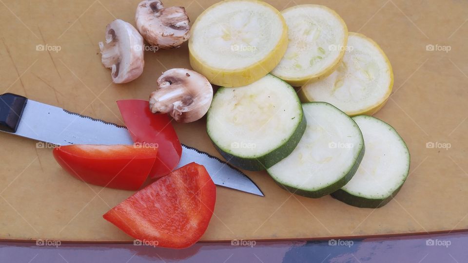 slices of red bell peppers cucumbers yellow squash mushrooms and stainless steel knife