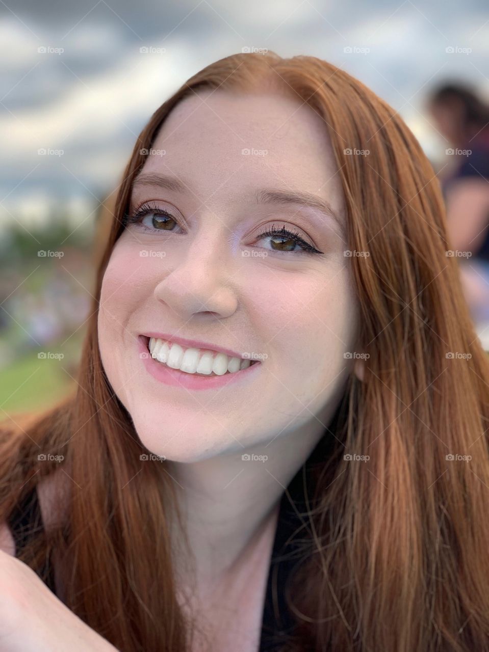 Beautiful redheaded model smiling directly into the camera at a music festival park type event