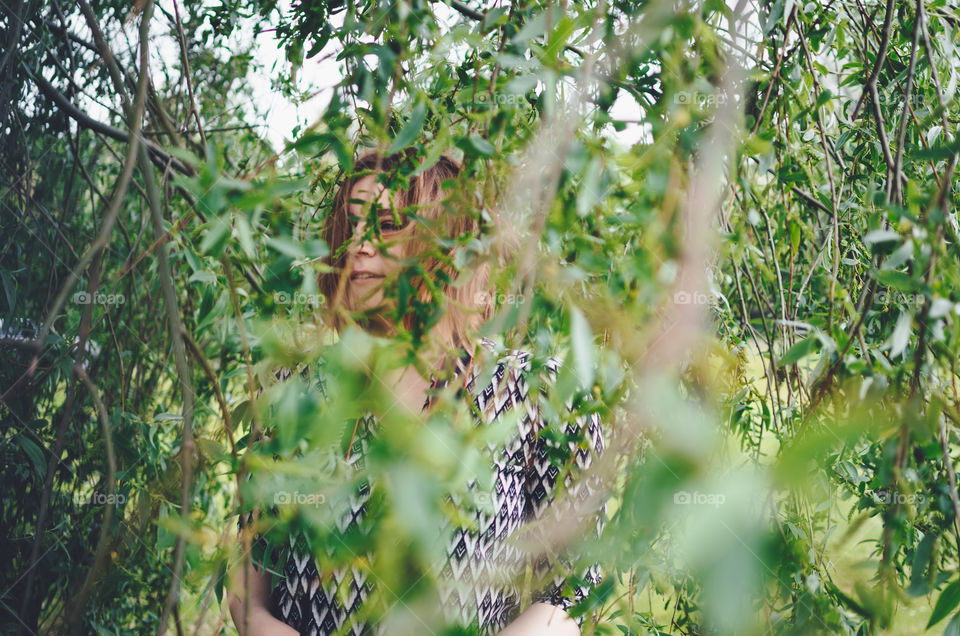 Beautiful ginger girl looking through the tree leaves.