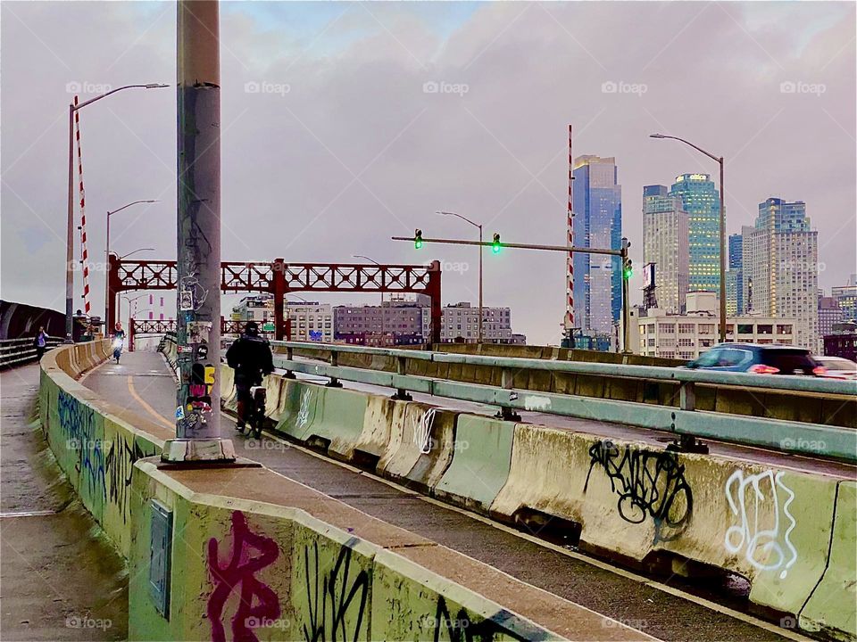 This is the „Pulaski Bridge“ seen from the pedestrian lane walking from „Greenpoint“, Brooklyn towards LIC, Queens. A bicyclist is speeding along on our right in the bicycle lane. 2023. Hypnotic Productions