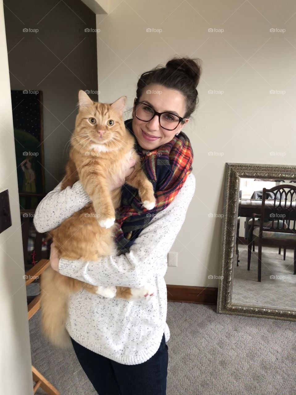Girl with glasses bun and scarf holding a Mainecoon long-haired orange large striped cat 