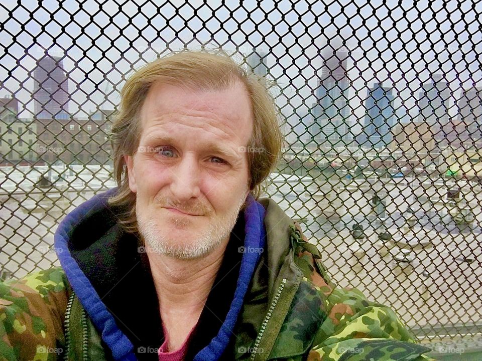 “Timothy Trespas” standing by a tall mesh fence in “Newtown Creek” by the “Pulaski Bridge” in the winter of 2019. Hypnotic Productions