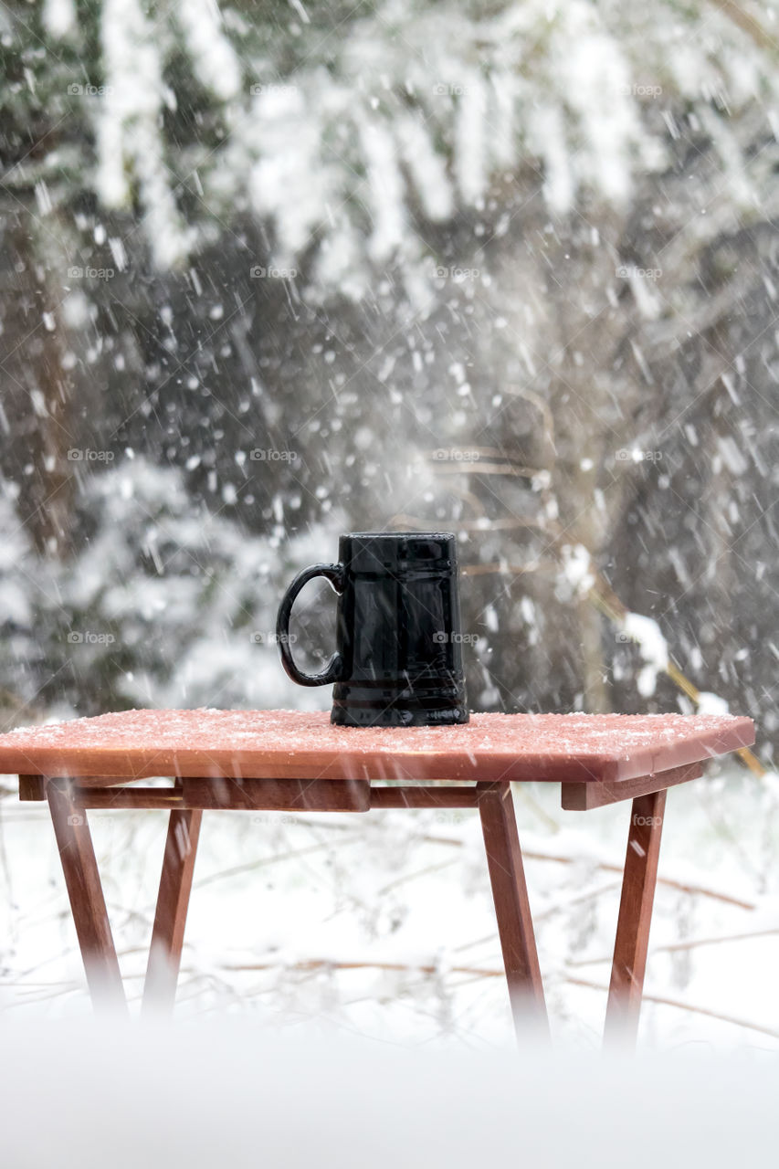 Medieval style black mug of hot steaming coffee, outside in a snowy winter wonderland scene.