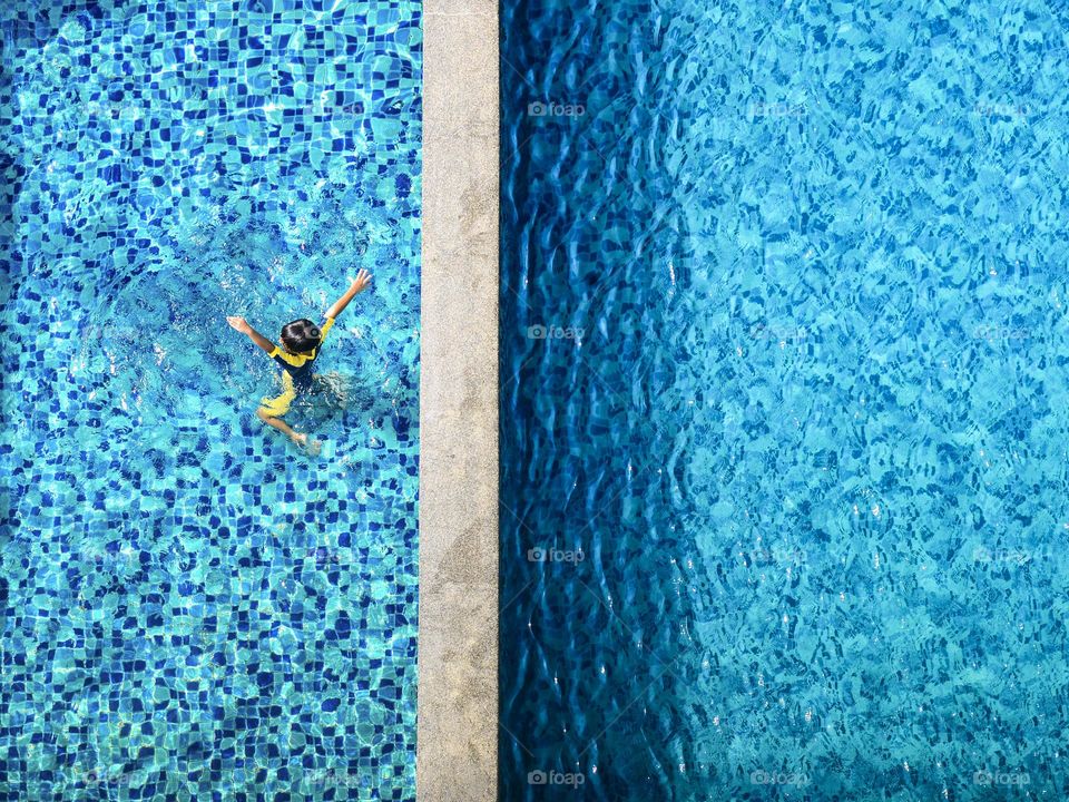 View from above of a boy playing in the swimming pool on a sunny day