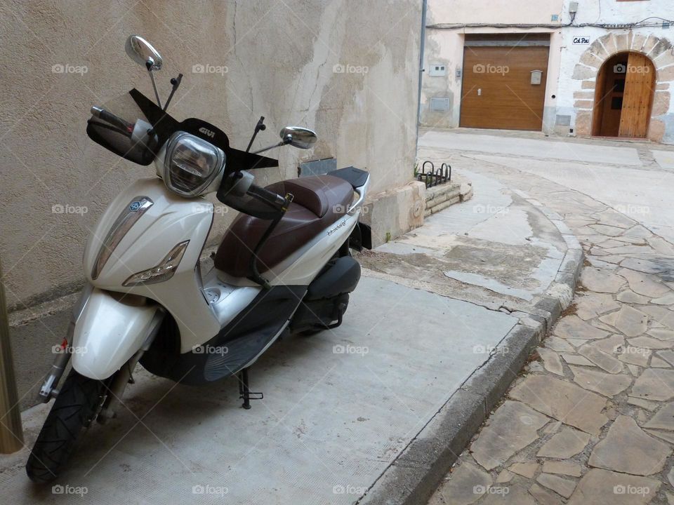 The scooter takes up little space and is easy to park for daily commutes. this photo shows a white scooter parked in front of a home