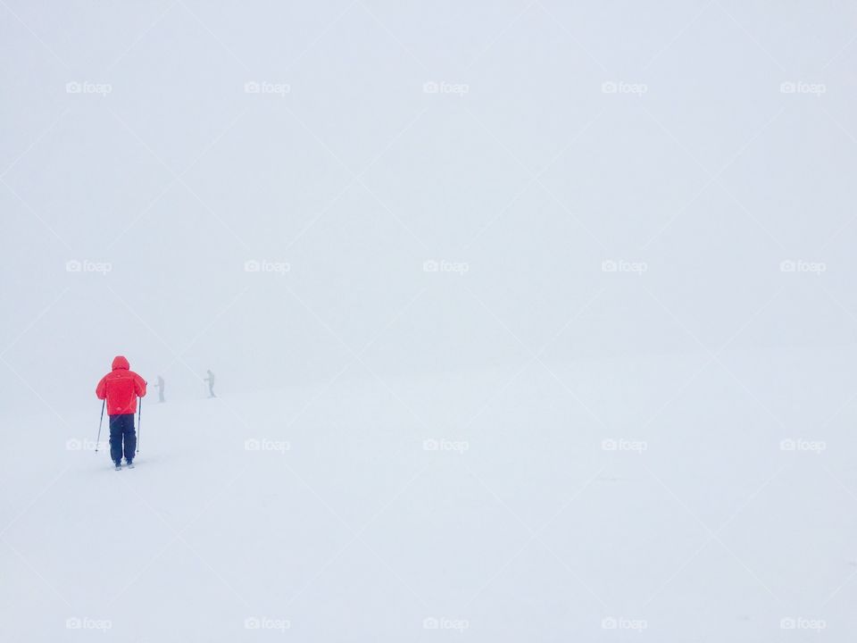 Skier in red ski jacket surrounded by fog and snow