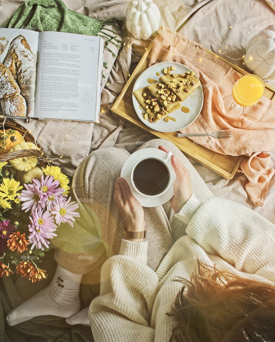 Girl having breakfast in bed and holding a cup of coffee, view from above