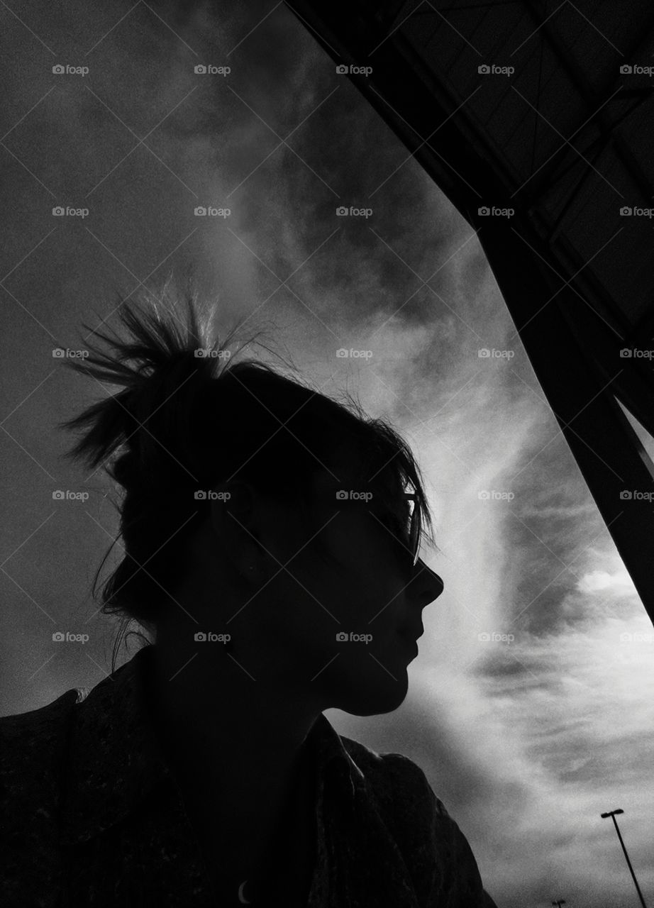 black and white of woman's side profile with a partially cloudy sky behind her