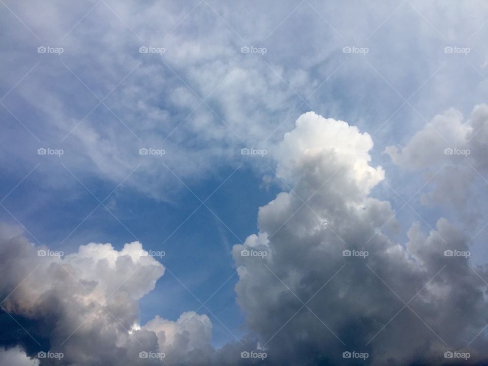 Towering storm clouds against a bright, blue sky with high, thin, wispy clouds