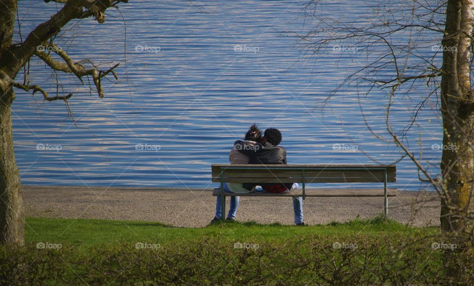 Young Couple Sitting In Front Of Lake At Dusk