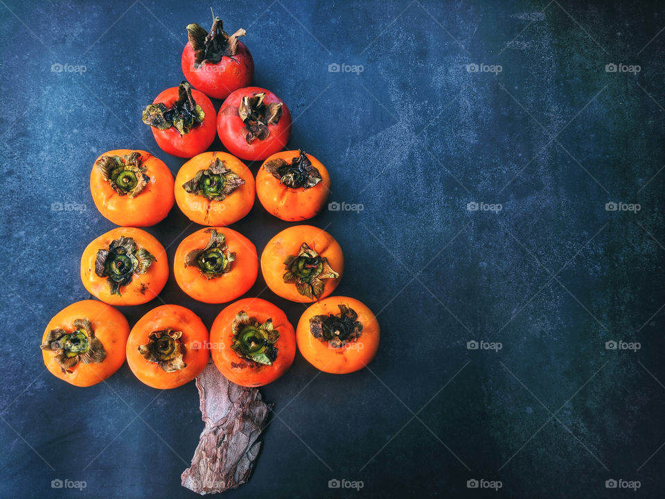 Christmas tree made of persimmon fruit on dark background close up. Funny food ideas for kids.