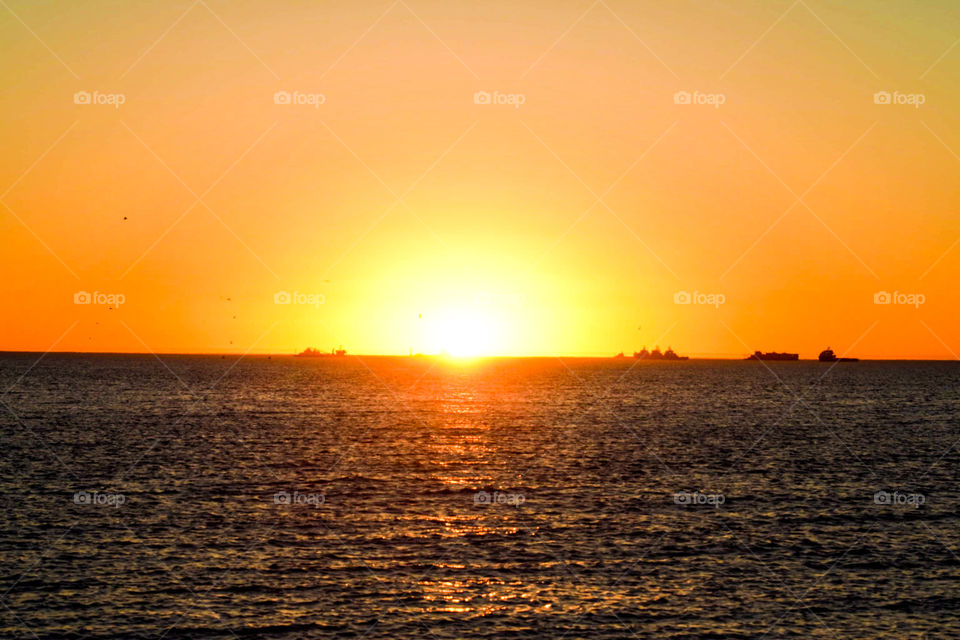 A beautiful golden sunset behind the ocean water of the Atlantic Ocean. With vessels on the water .