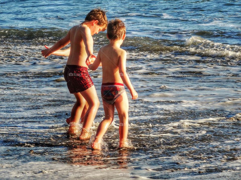 Three Boys In The Ocean Shallows. Young Brothers At The Beach