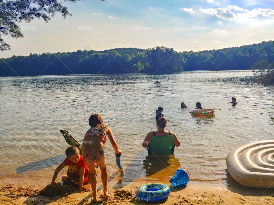 A group of people spending the day floating in the lake and building sandcastles on the beach.