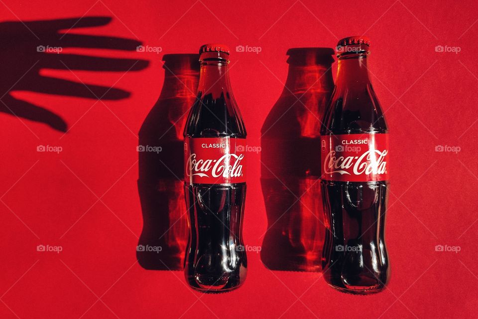 two bottles of coca cola and hand shadow on red background