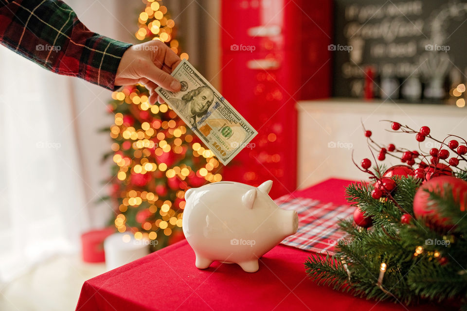 piggy bank with 100 dollars banknote in festive New Year atmosphere of scenery.  Magical bokeh with Christmas tree and bright lights.