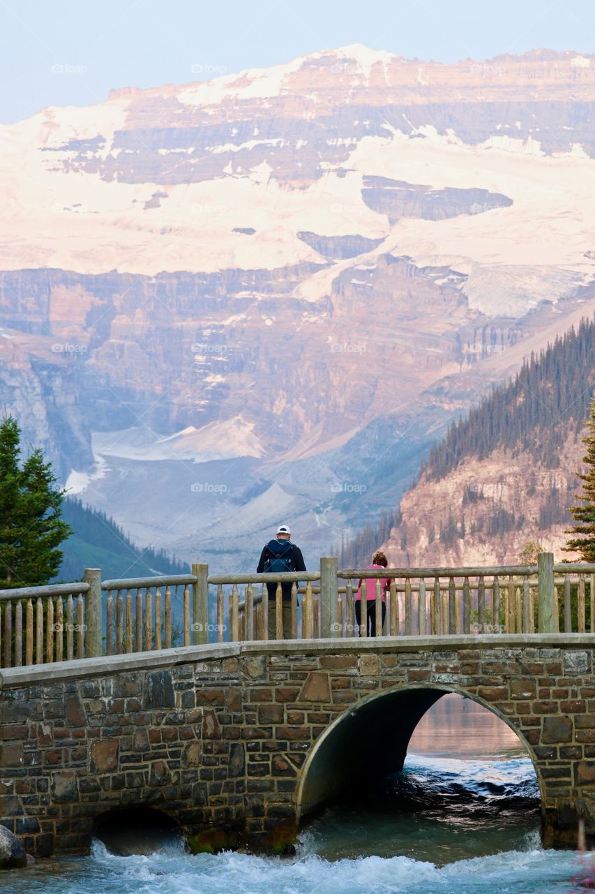 Man taking in view from romantic bridge overlooking Lake Louise and Canada's Rocky Mountains 