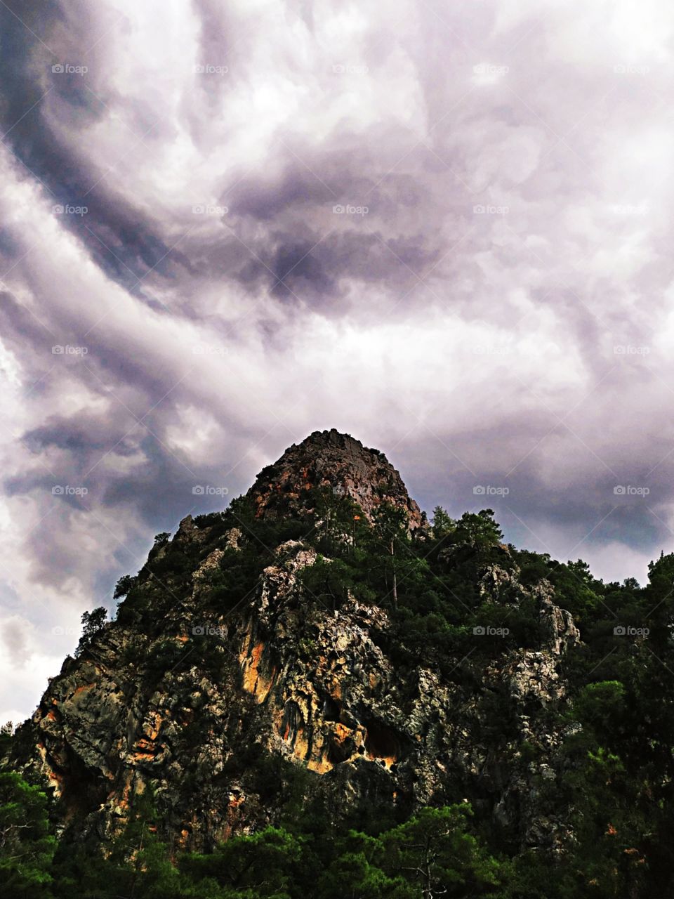 A mountain with trees and background with scary pre-storm clouds on the sky.