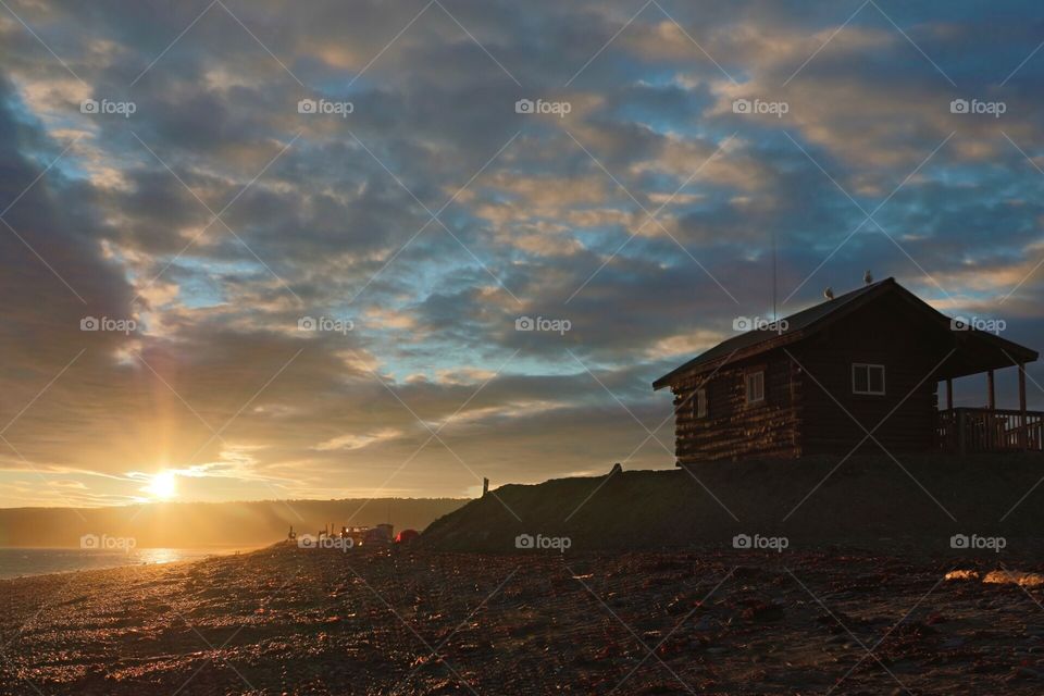 Beachfront Cabin. A small log cabin sits on the beach in Alaska.  A beautiful setting as the sun goes down. 