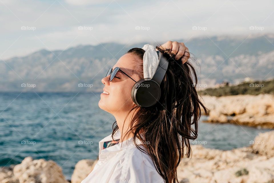 Young woman enjoying listening to music on heaphones on a beach in summer