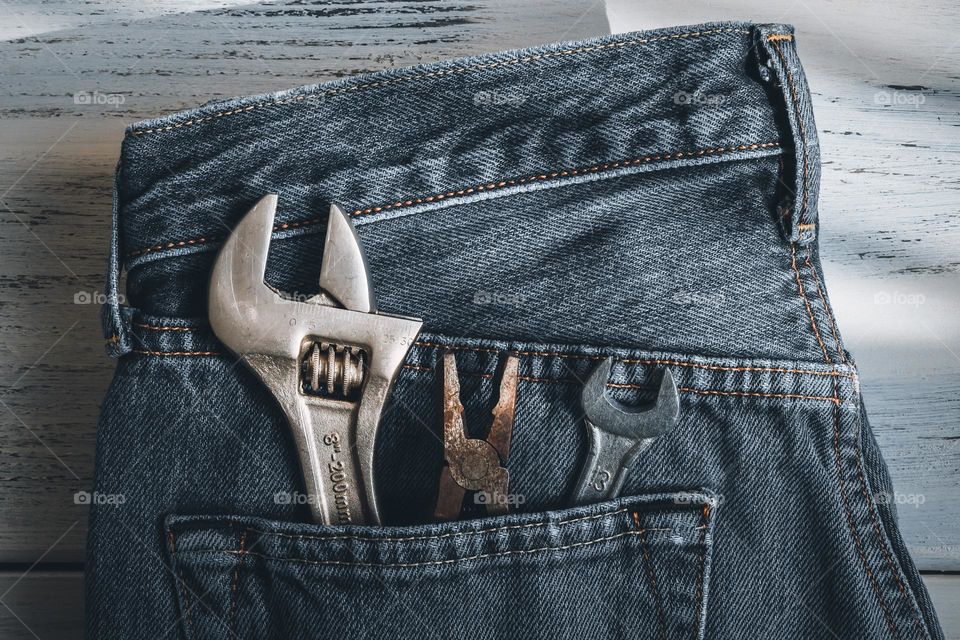 Metal tools pliers, an adjustable wrench and a wrench lie in a male jeans pocket on a white wooden shabby table, flat lay close-up. The concept of tools,metal,father's day.