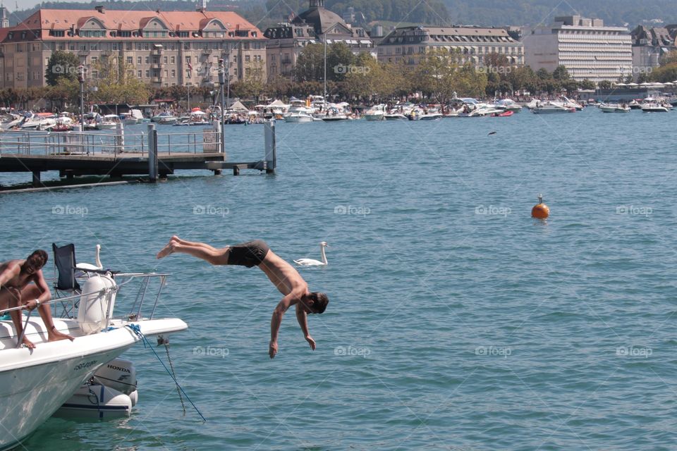 Diving. Young man jumping off of boat to dive into lake water in Zürich,Switzerland.