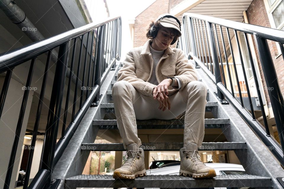 Boy sitting on stairs looking at his apple watch and is wearing headphones 