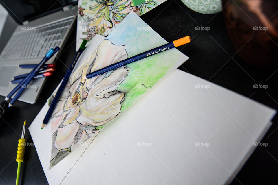 Low angle view of Faber-Castell Art Grip Aquarelle Colored watercolor pencils sketch closeup spring flower with sketchbook on table with laptop and coffee conceptual work life balance, creativity, hobby artist lifestyle photography