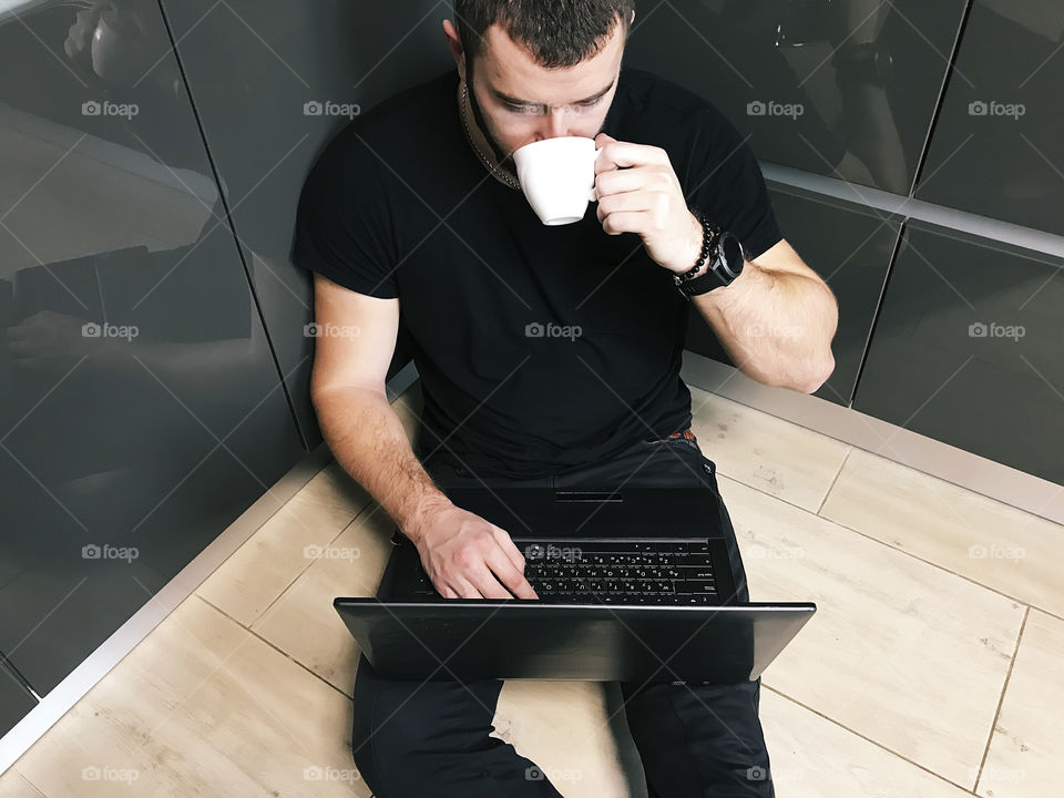 Young man with smart watches using social media at his favorite laptop while drinking morning coffee at home 