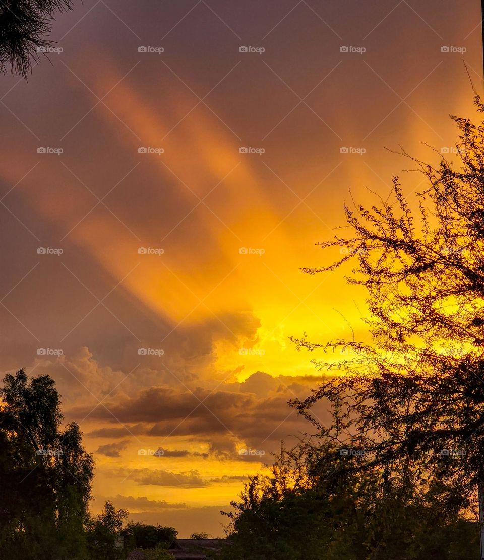 Radiant sunbeams erupt from behind dense clouds during a Arizona monsoon creating orange highlights in the sky