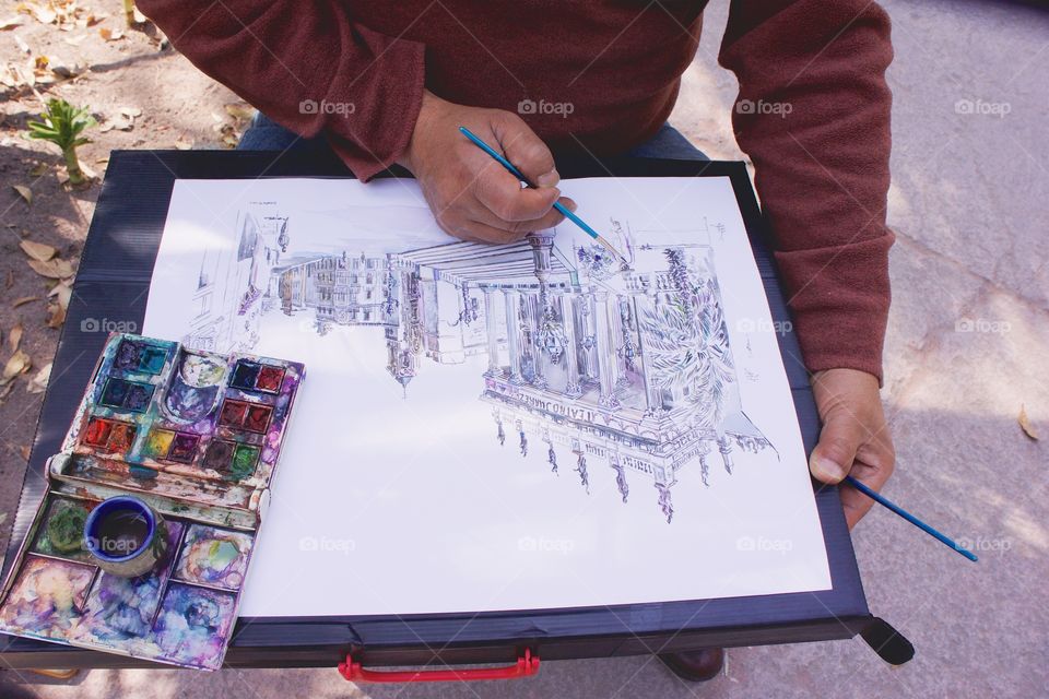 A painter sits in a park in San Miguel de Allende, Mexico painting in water colors a scene from Guanajuato, Mexico.