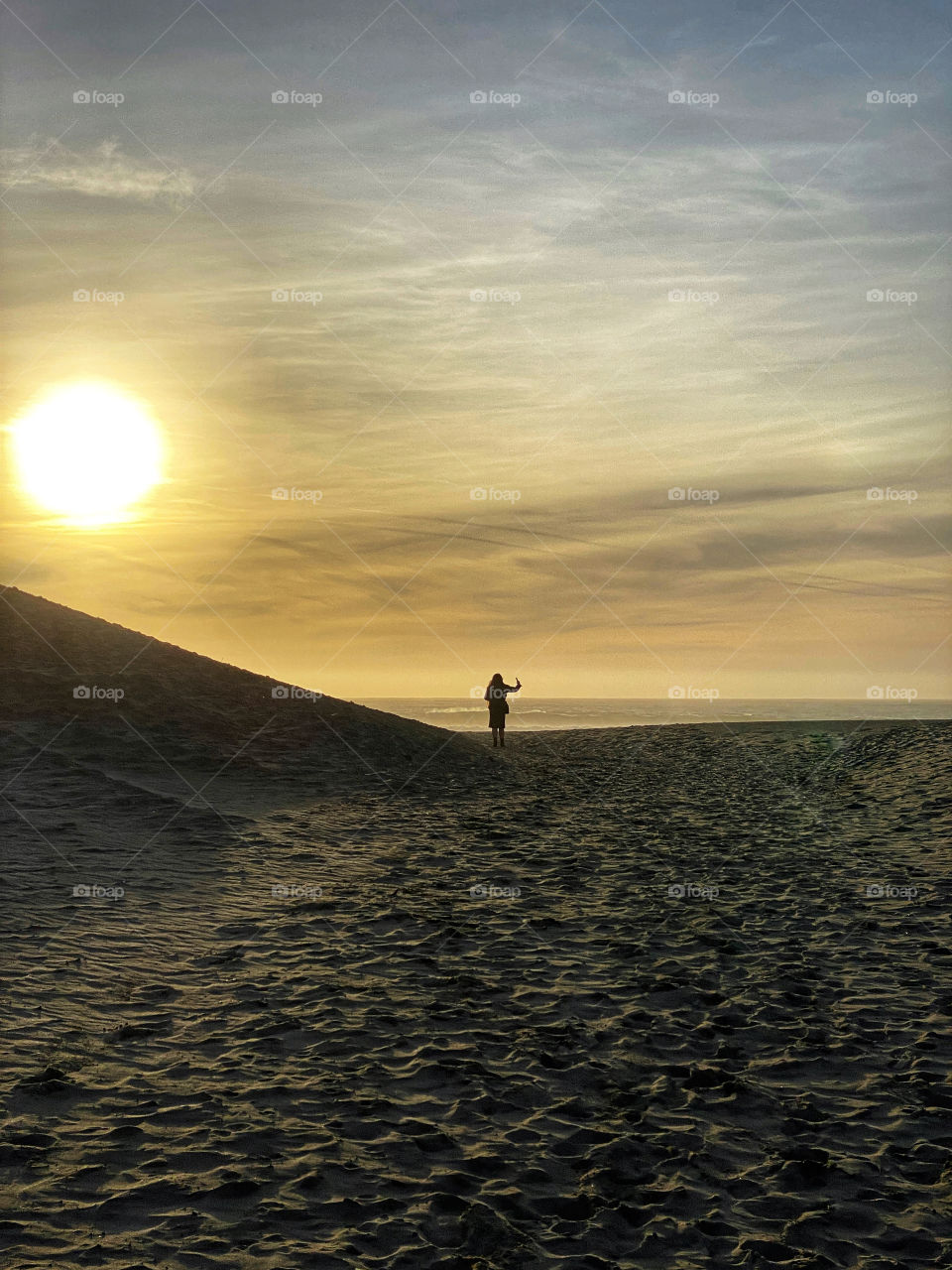 Silhouette of a woman taking a selfie on a beach at sunset 