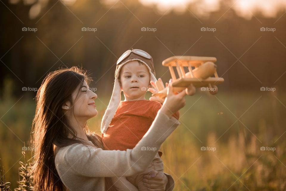 Mother with son playing with wooden plane at sunset