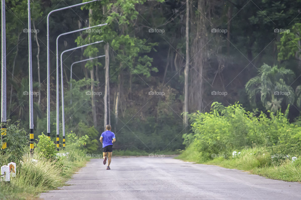 The men are running on the road Background light poles and trees.