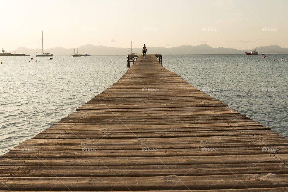 Woman walking on wooden pier in the ocean at sunrise 