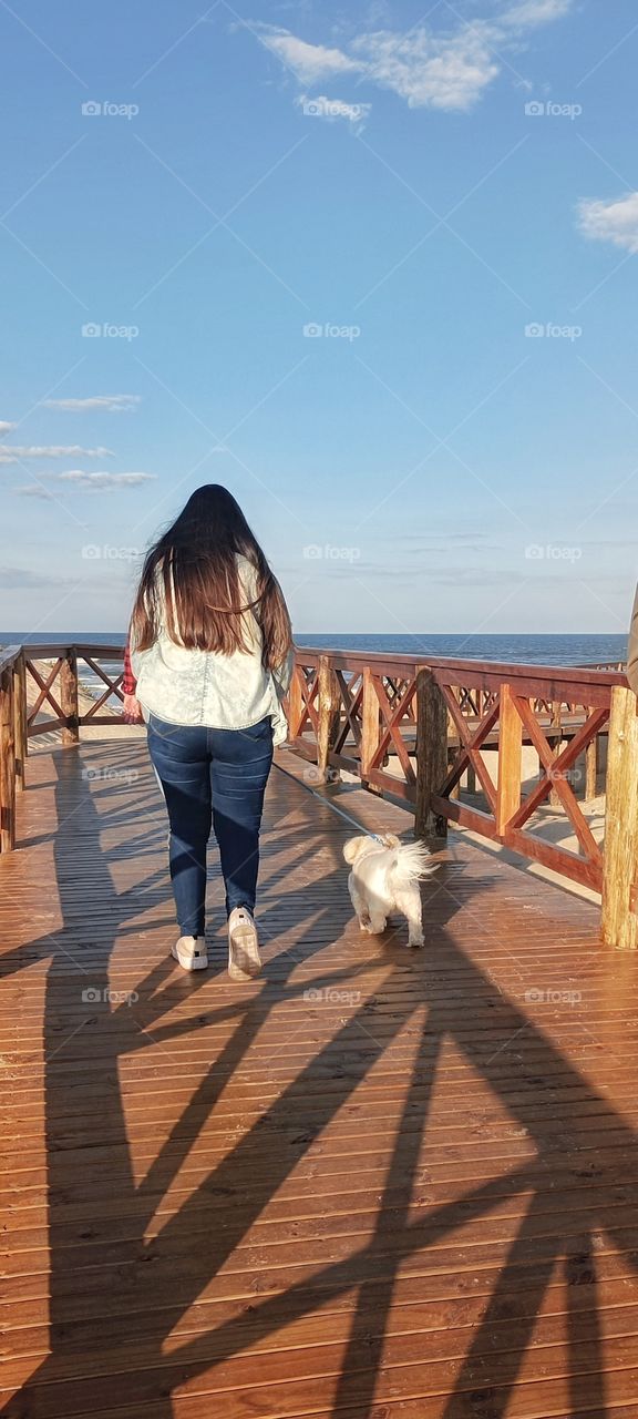 Girl walking her pet in the morning by the sea.