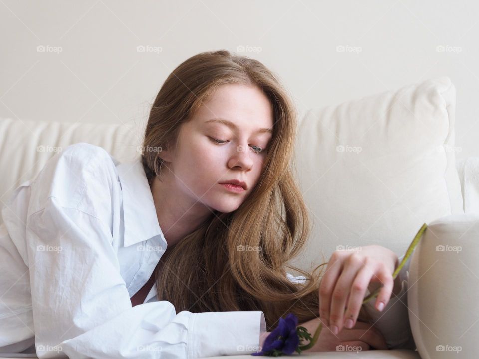 Young beautiful girl with long blonde hair lies on a white sofa 