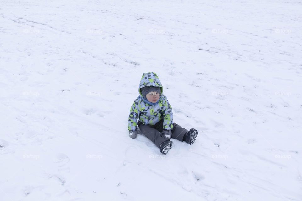 A small, carefree boy walks in winter through the white snow in the park, near the trees in the snow.