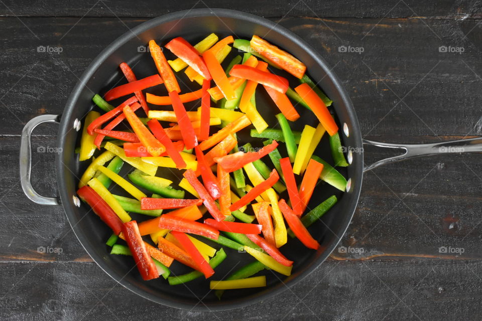 Colorful raw julienned bell peppers in a skillet on a wood background 