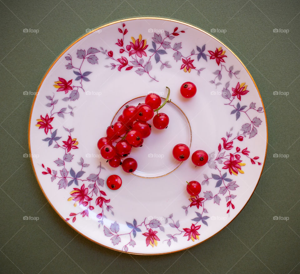 Red currant berries on a porcelain ornamental saucer on a dark background.  Healthy food
